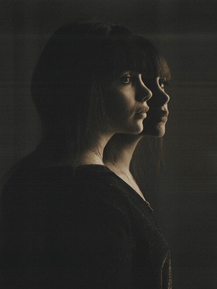 Two Gemini woman with emotionless expressions facing sideways on dark background.