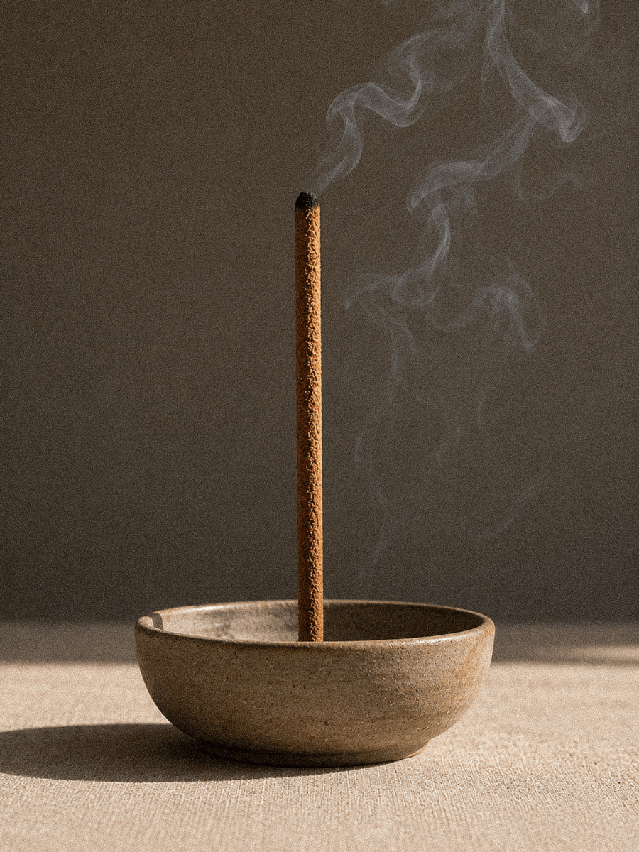 Hand Rolled Palo Santo incense stick burning in a ceramic bowl with smoke against a dark background.