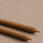 Two hand rolled Palo Santo incense sticks up close on a neutral surface.