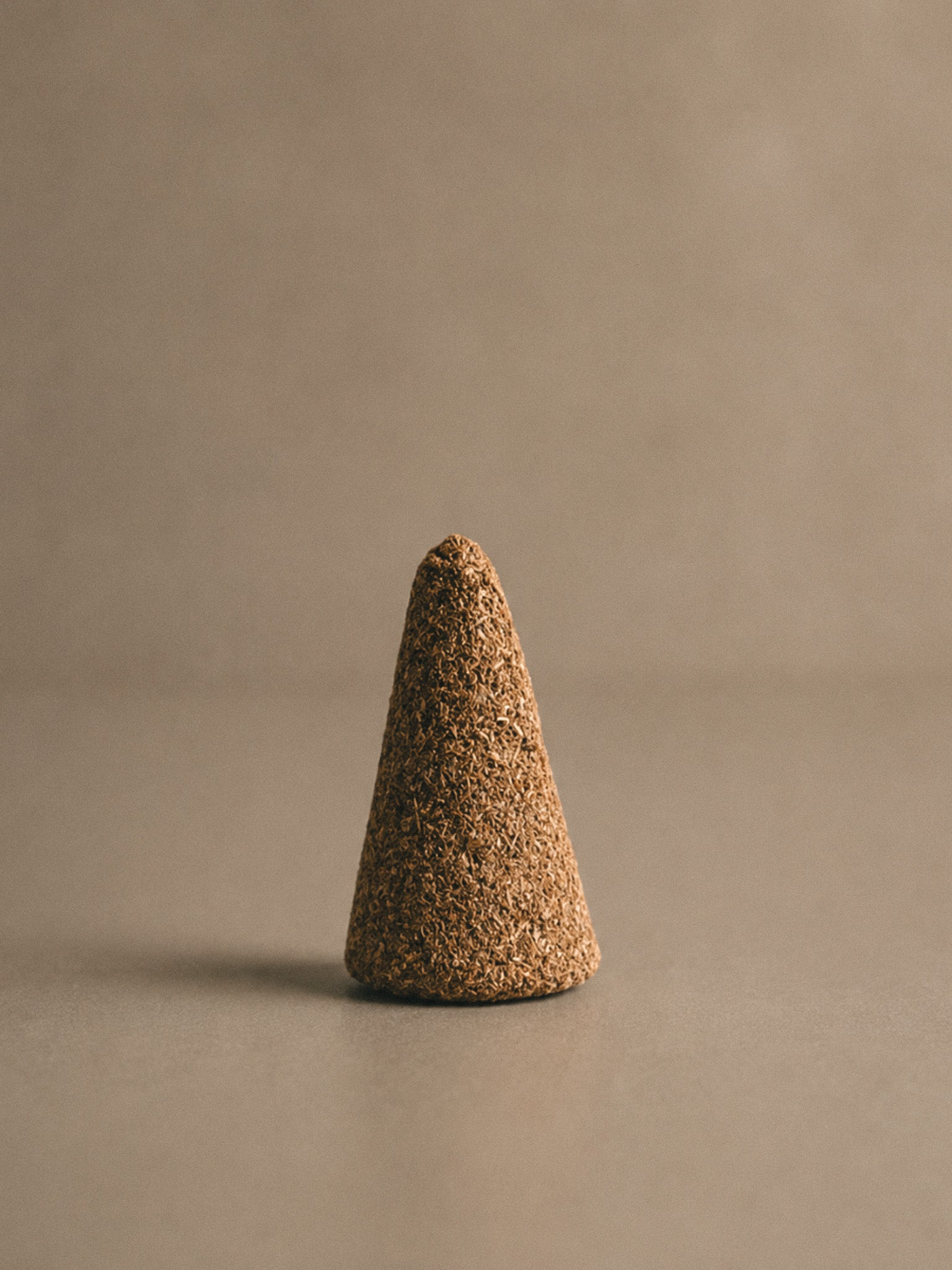 Close up of a Palo Santo incense cone on a neutral background.