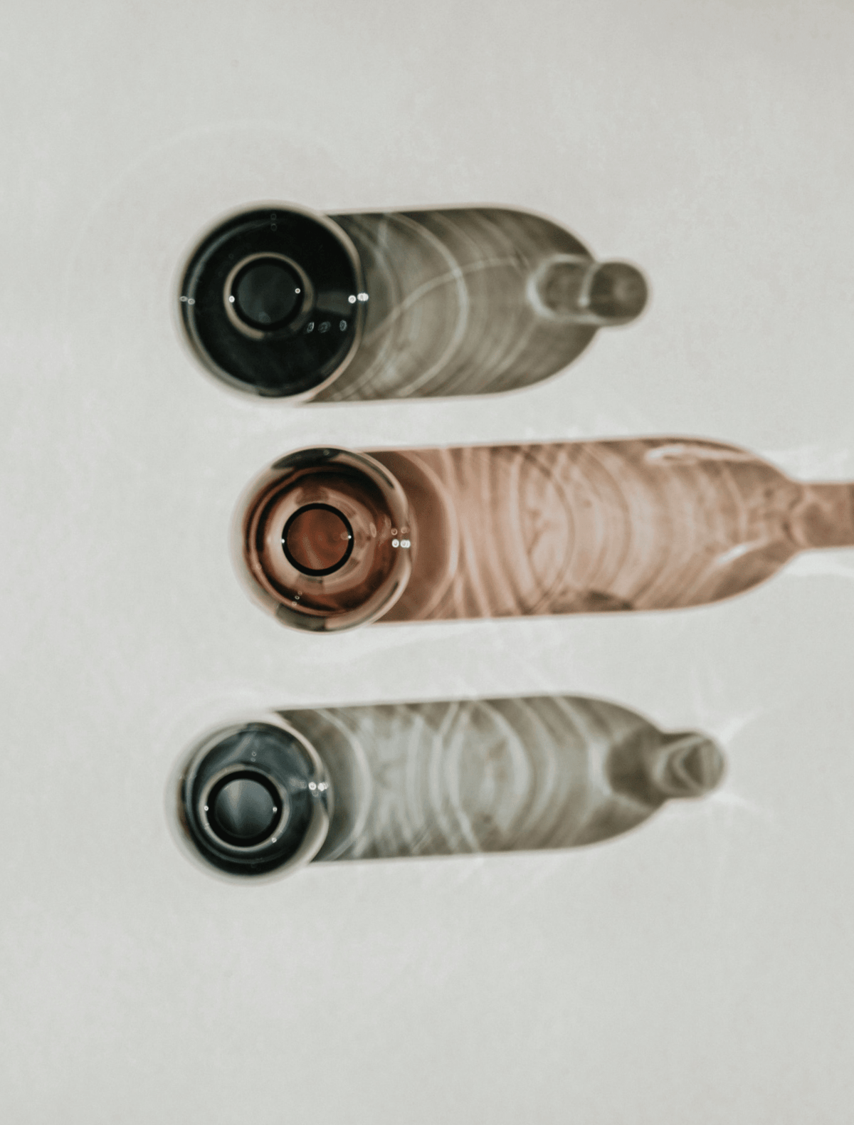 Three glass bottles in charcoal, dusty rose, and smoky gray stacked against off-white, the study image for the Interval candle