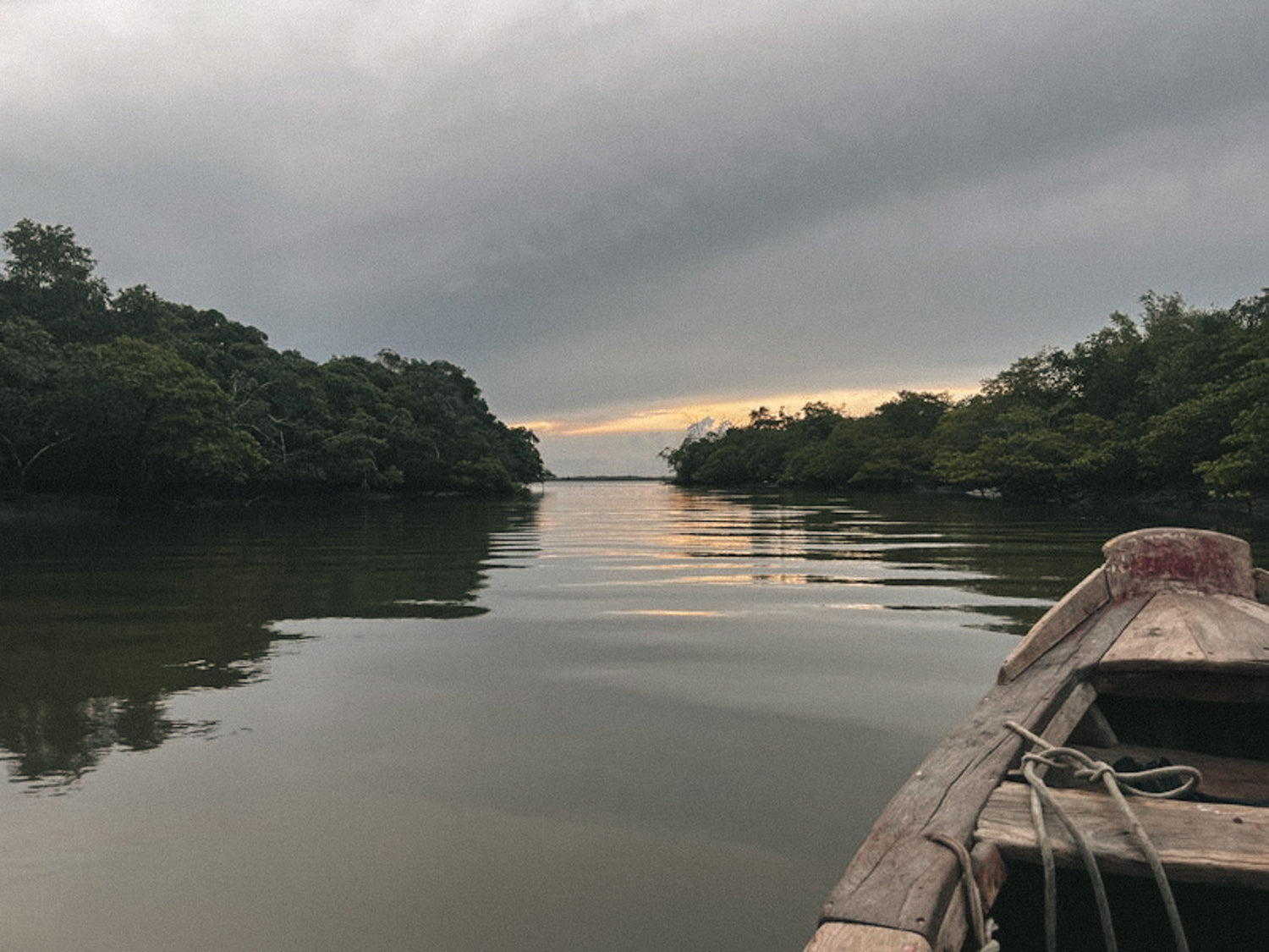 Wooden boat on a river with trees and a cloudy sky.