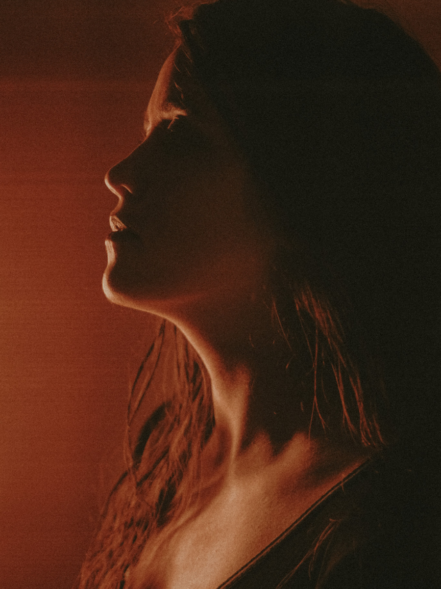 Leo woman with fiery red hair with a powerful expression against a red lit background.