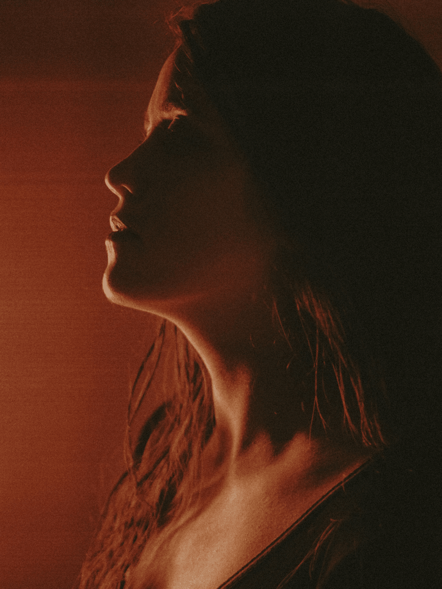 Leo woman with fiery red hair with a powerful expression against a red lit background.