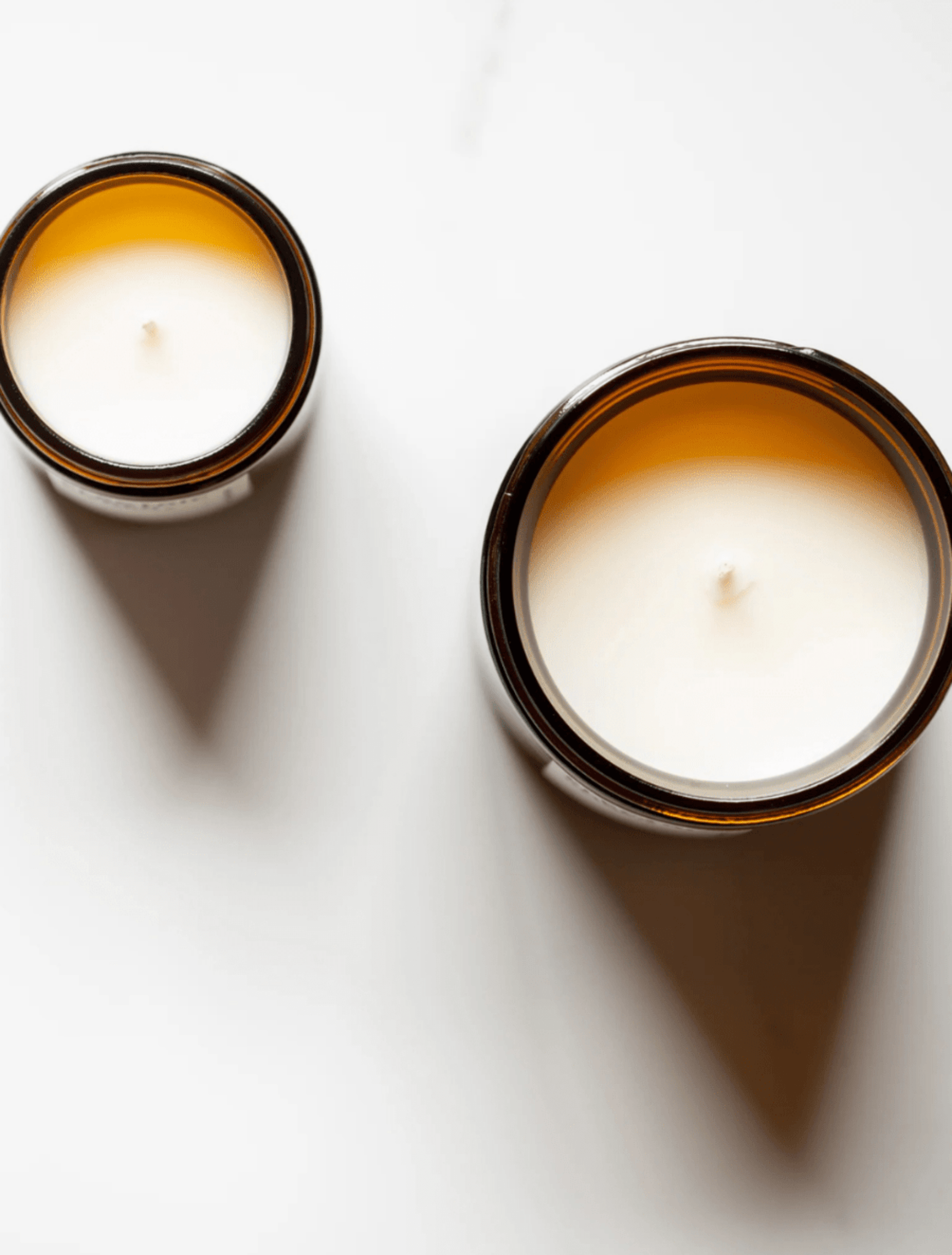 Two amber glass jar candles with white coconut apricot wax, photographed from above on a clean white surface with soft shadows.