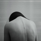 A Libra woman with her bare back and looking down in defeated position against a neutral gray background.