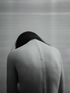 A Libra woman with her bare back and looking down in defeated position against a neutral gray background.