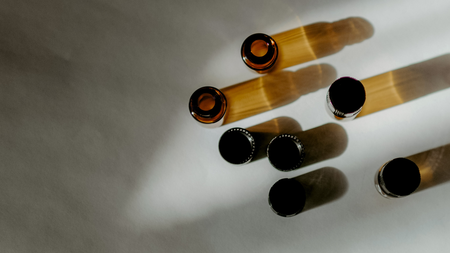 A set of glass amber bottles from above with shadows on a neutral background.