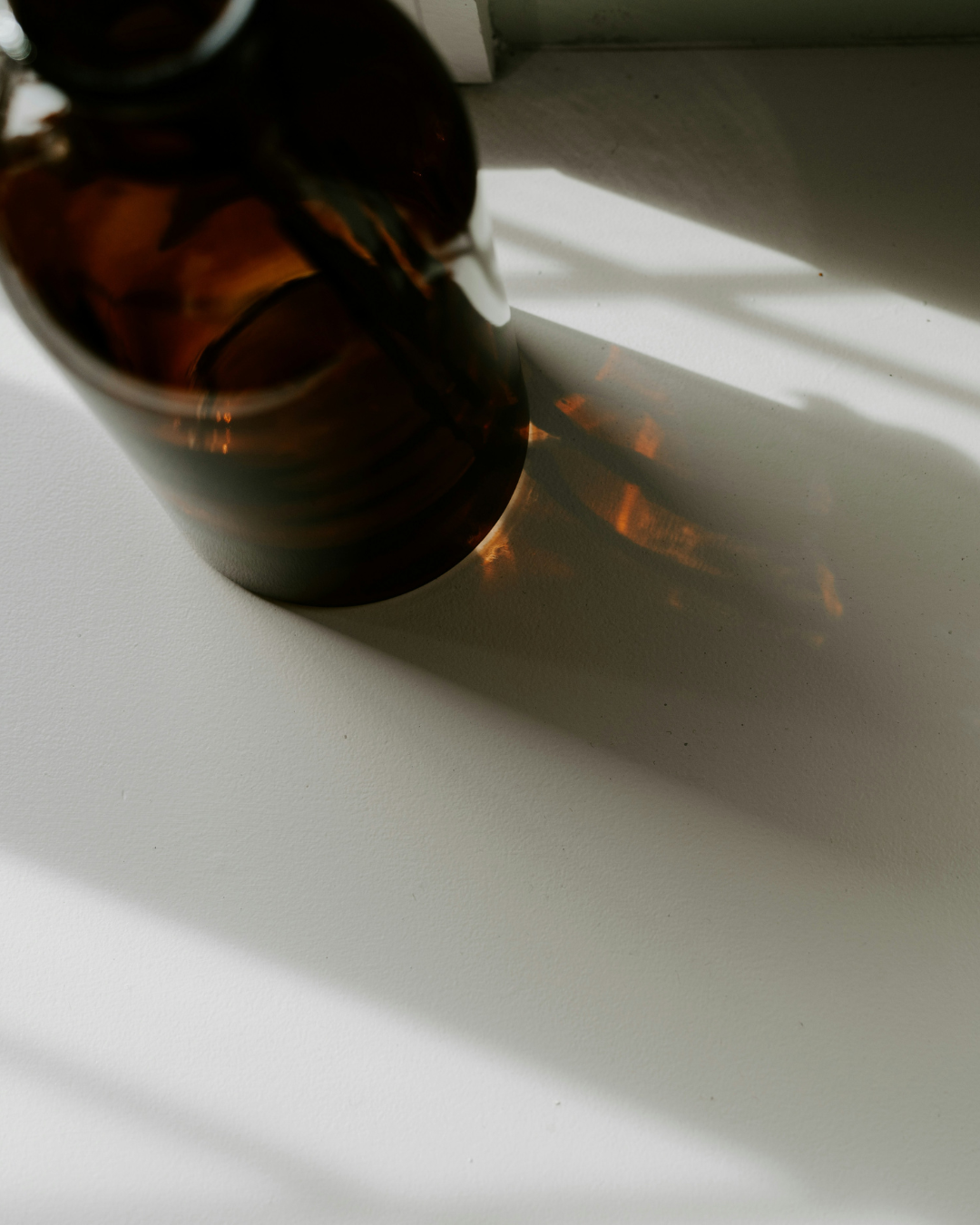 Brown glass fragrance bottle on a white surface with a shadow cast by the container.