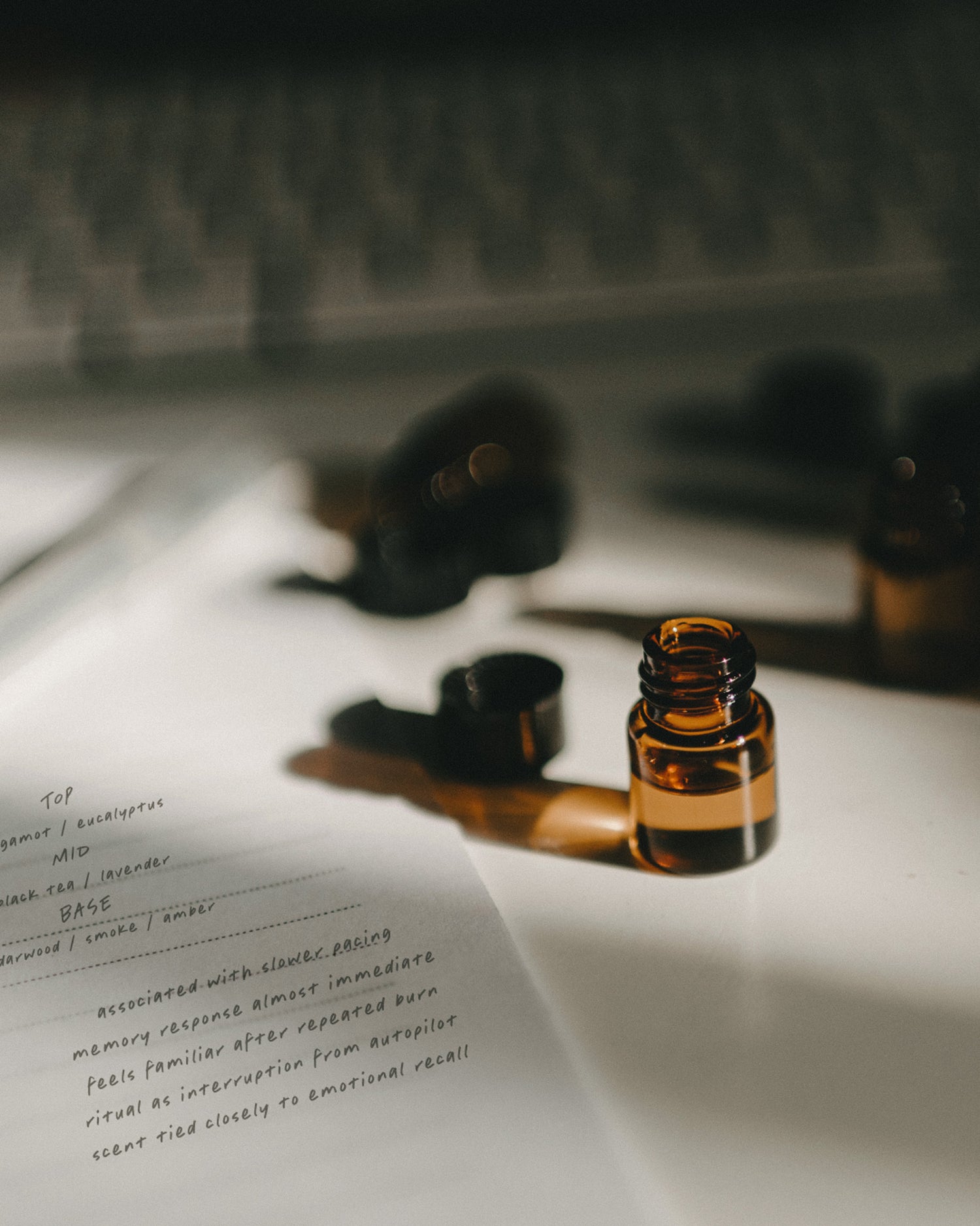 Open bottle of fragrance oil sample next to a notepad with handwritten notes with a blurred keyboard in the background.