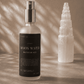 Bottle of 'Moon Water' meditation mist next to a crystal tower on a textured surface with sunlight casting shadows.