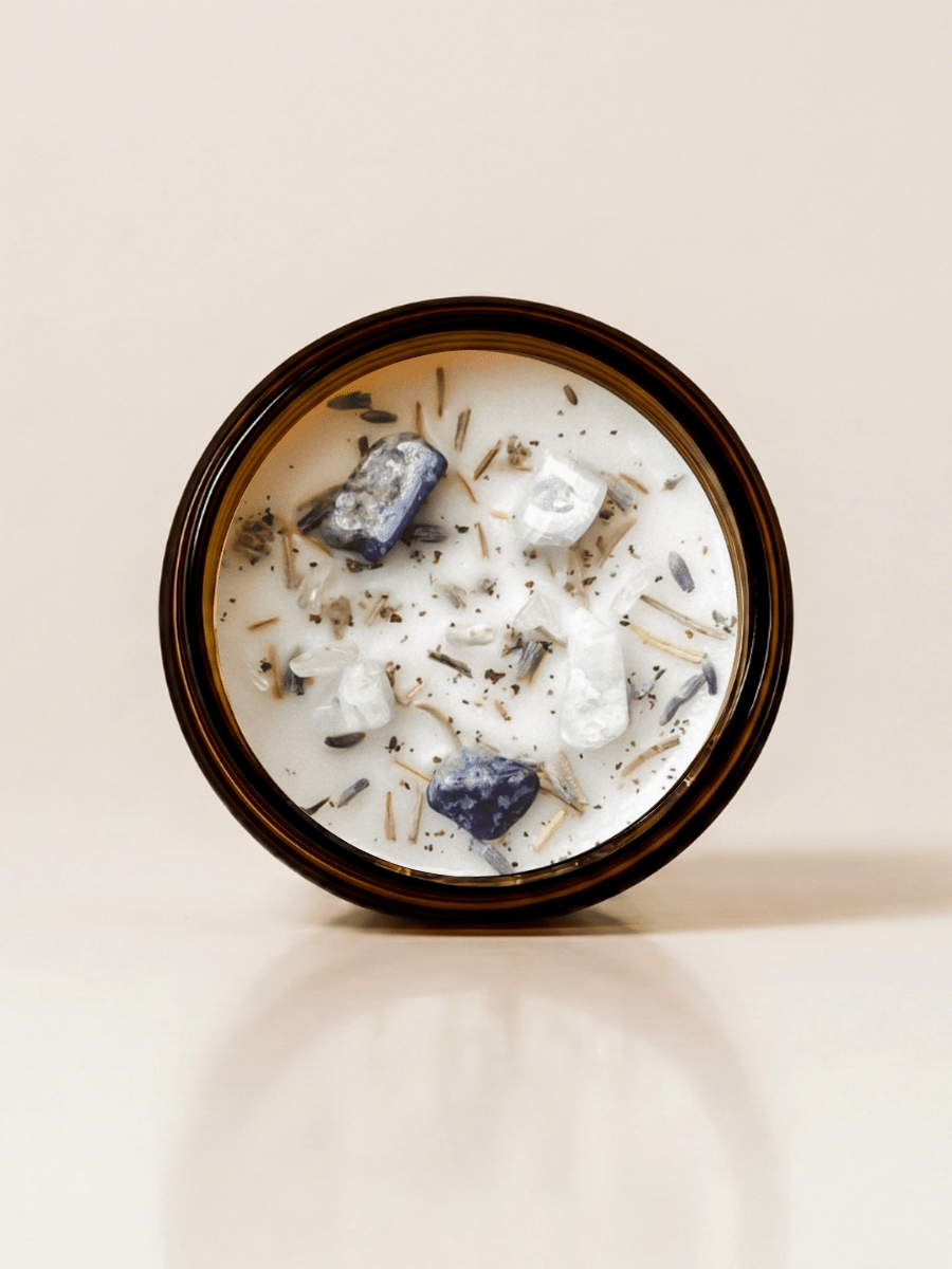 New Moon ritual candle with lapis lazuli, moonstone, quartz, and botanical details viewed from above.