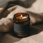 Orange Blossom + Clove Bare candle burning beside soft linen in warm atmospheric light.