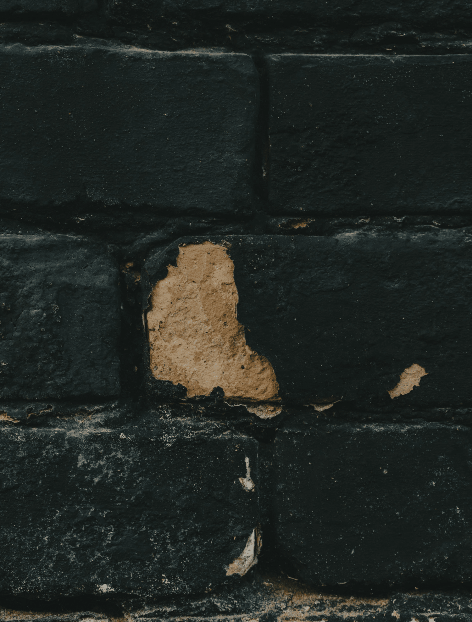 A close-up of a black painted brick wall with a rough, exposed tan plaster section in the center.