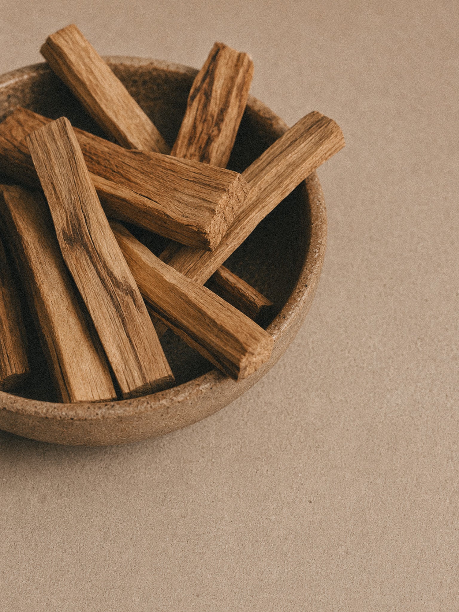 Wooden bowl of Palo Santo sticks on a neutral background.