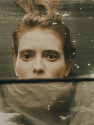 A Pisces woman underwater wide eyed and pensive.