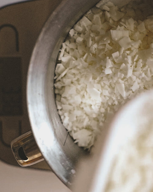 Flakes of coconut apricot wax being poured into an aluminum container, sitting on top of a scle.