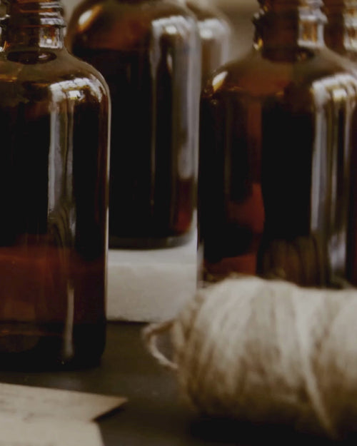 Close up editorial video of amber fragrance bottles, and a pool of cotton wick on a neutral background.