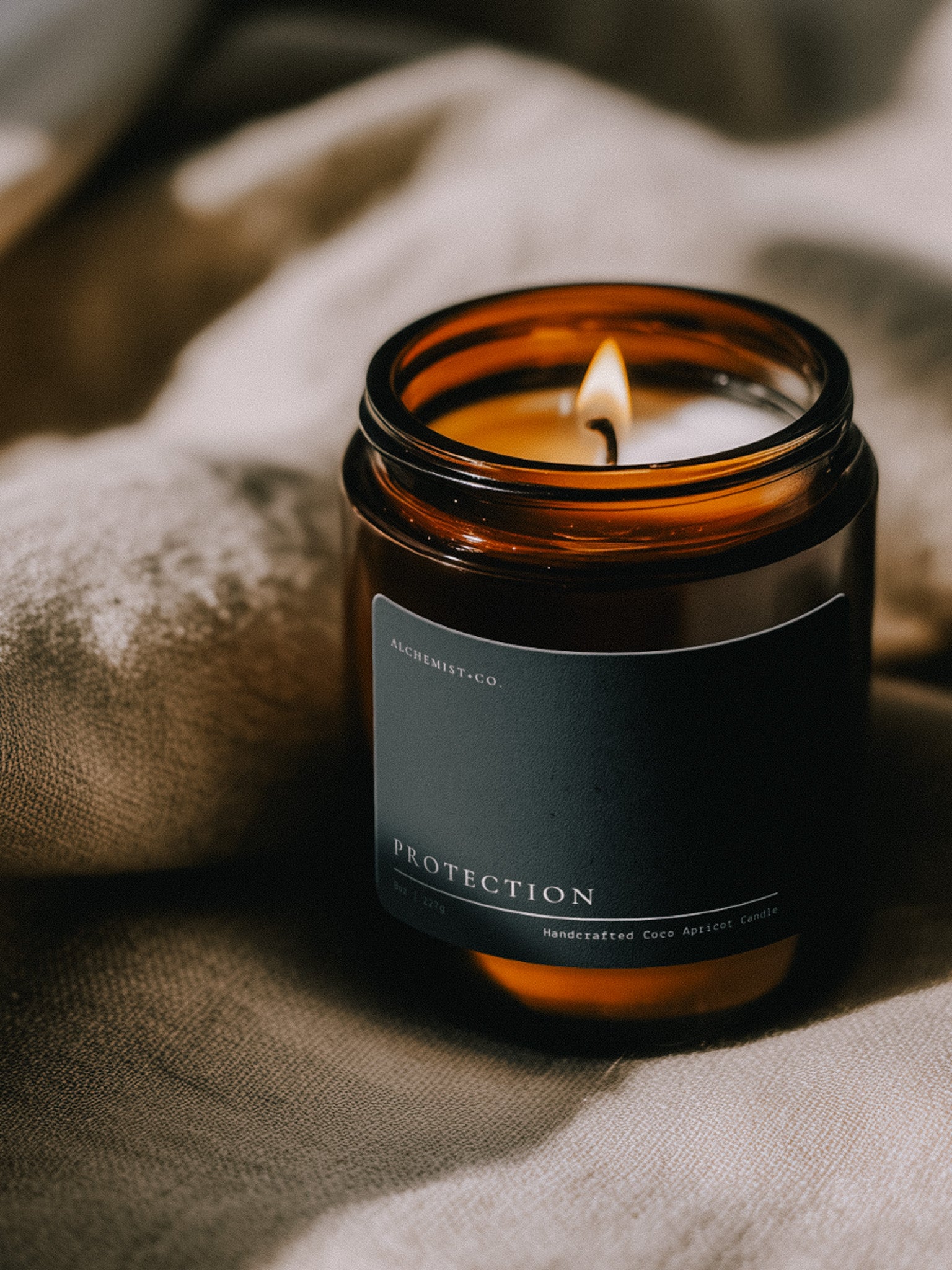 Lit Protection ritual candle beside textured linen in warm atmospheric light.