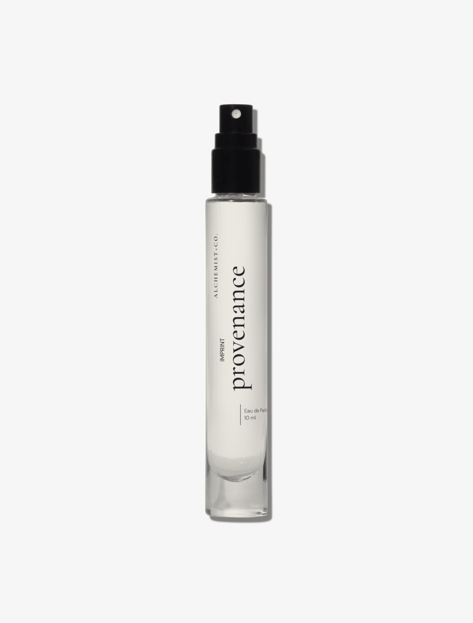 A clear glass perfume bottle featuring a white label with the brand name 'Provenance' by Alchemist + Co.  set against a solid light gray background.
