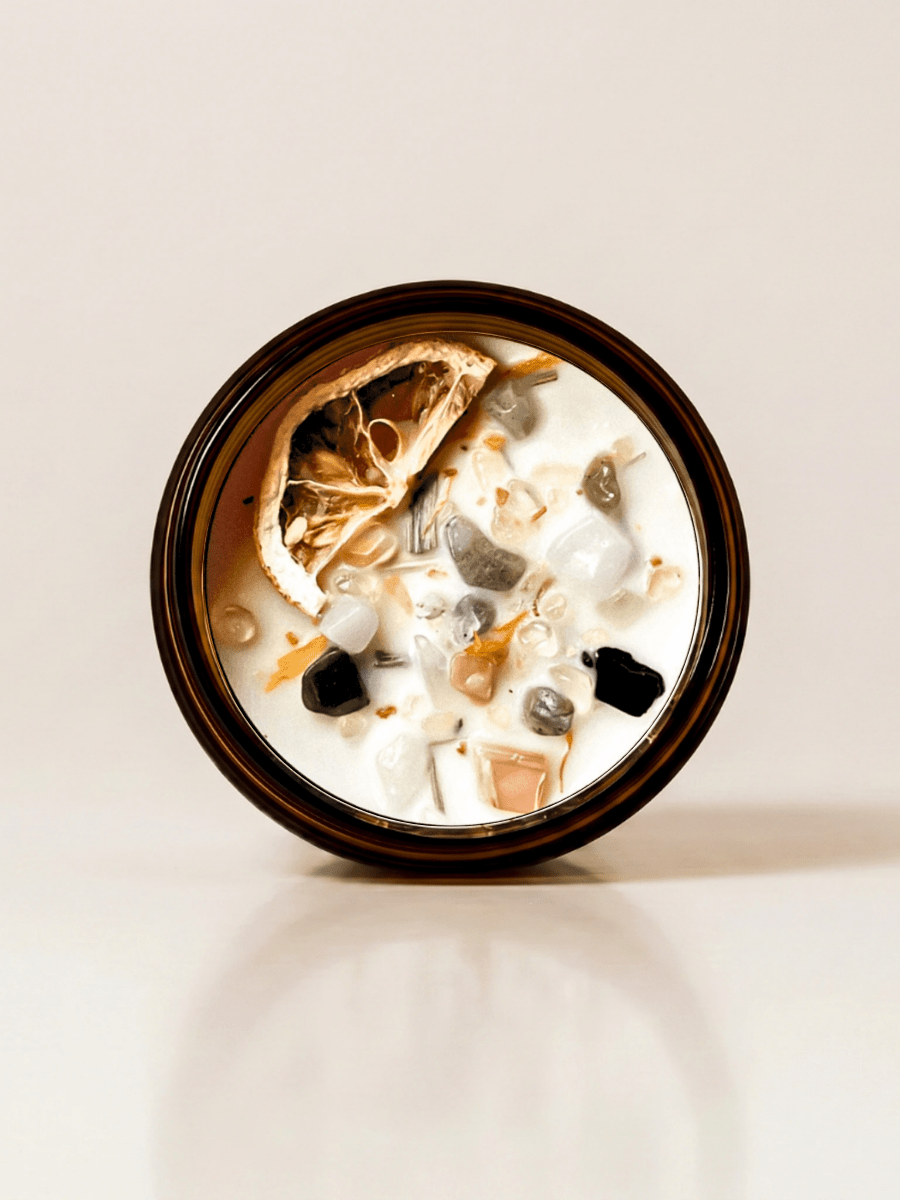 Renewal ritual candle with moonstone, black tourmaline, rutilated quartz, and botanical details viewed from above.
