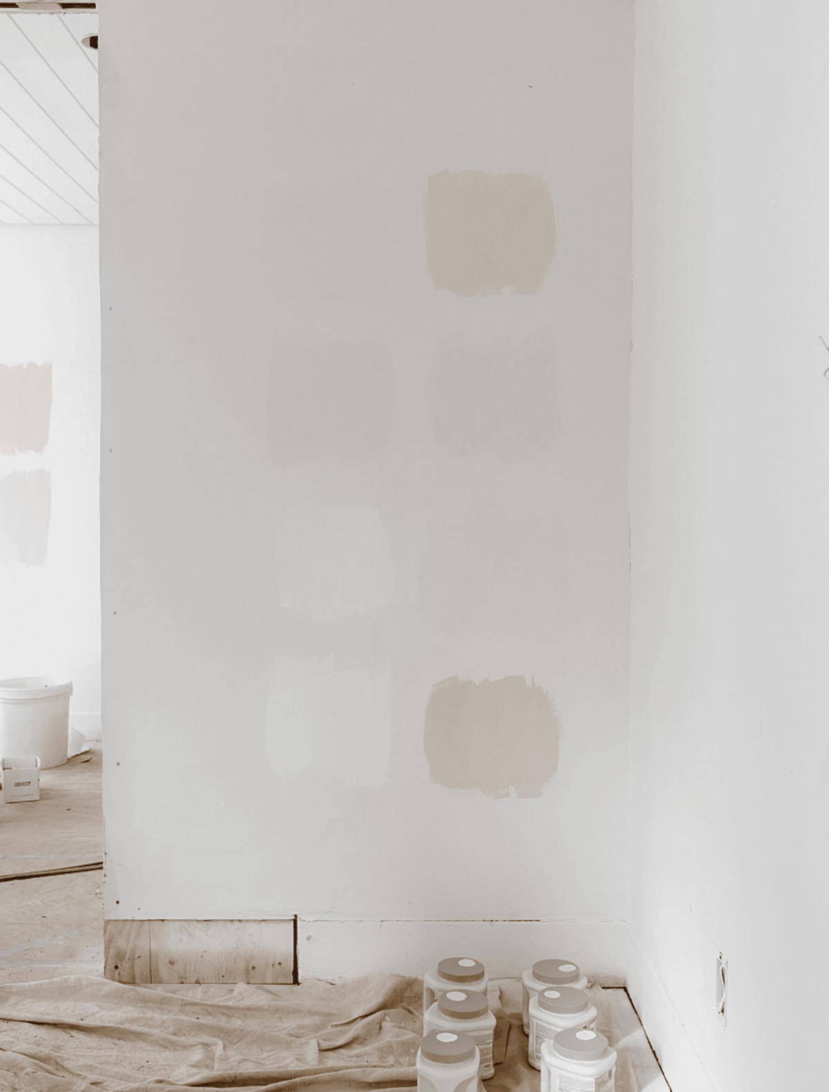 Neutral paint swatches on a white wall above paint cans and a drop cloth, the study image for the Revision candle