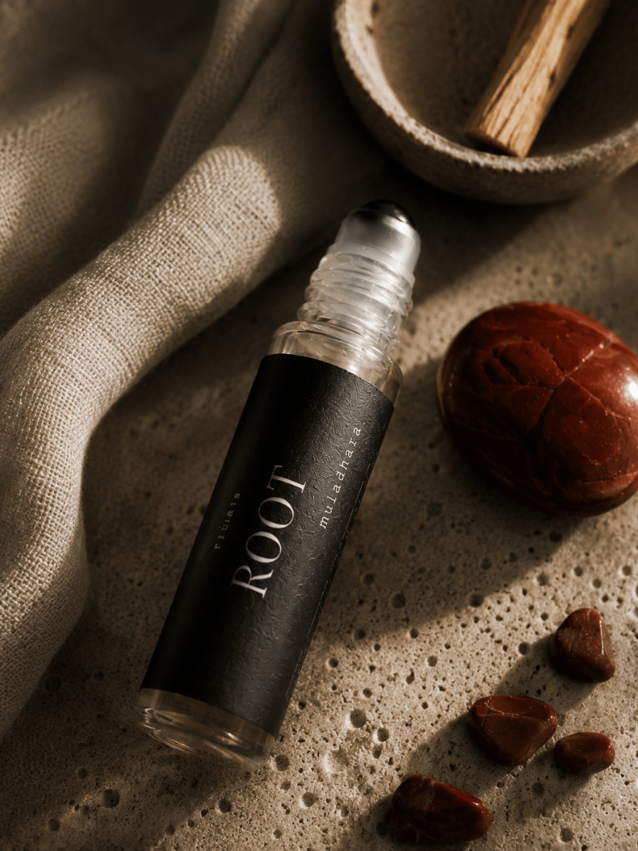 Roll-on bottle labeled Root Chakra Balancing Roller by Alchemist + Co.  on a textured surface with natural elements.