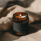 Rosemary + Cedar Sage Bare candle burning beside soft linen in warm atmospheric light.