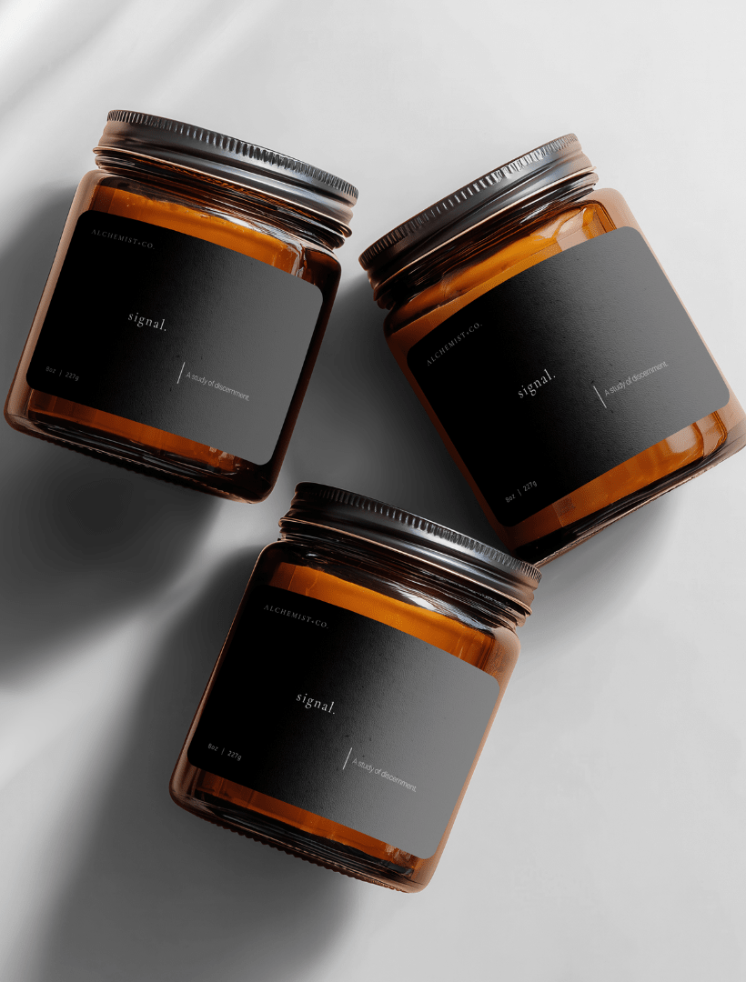 Three amber glass jar candles with black labels and silver lids, arranged diagonally on a light gray background with soft shadows labeled 'Signal'.