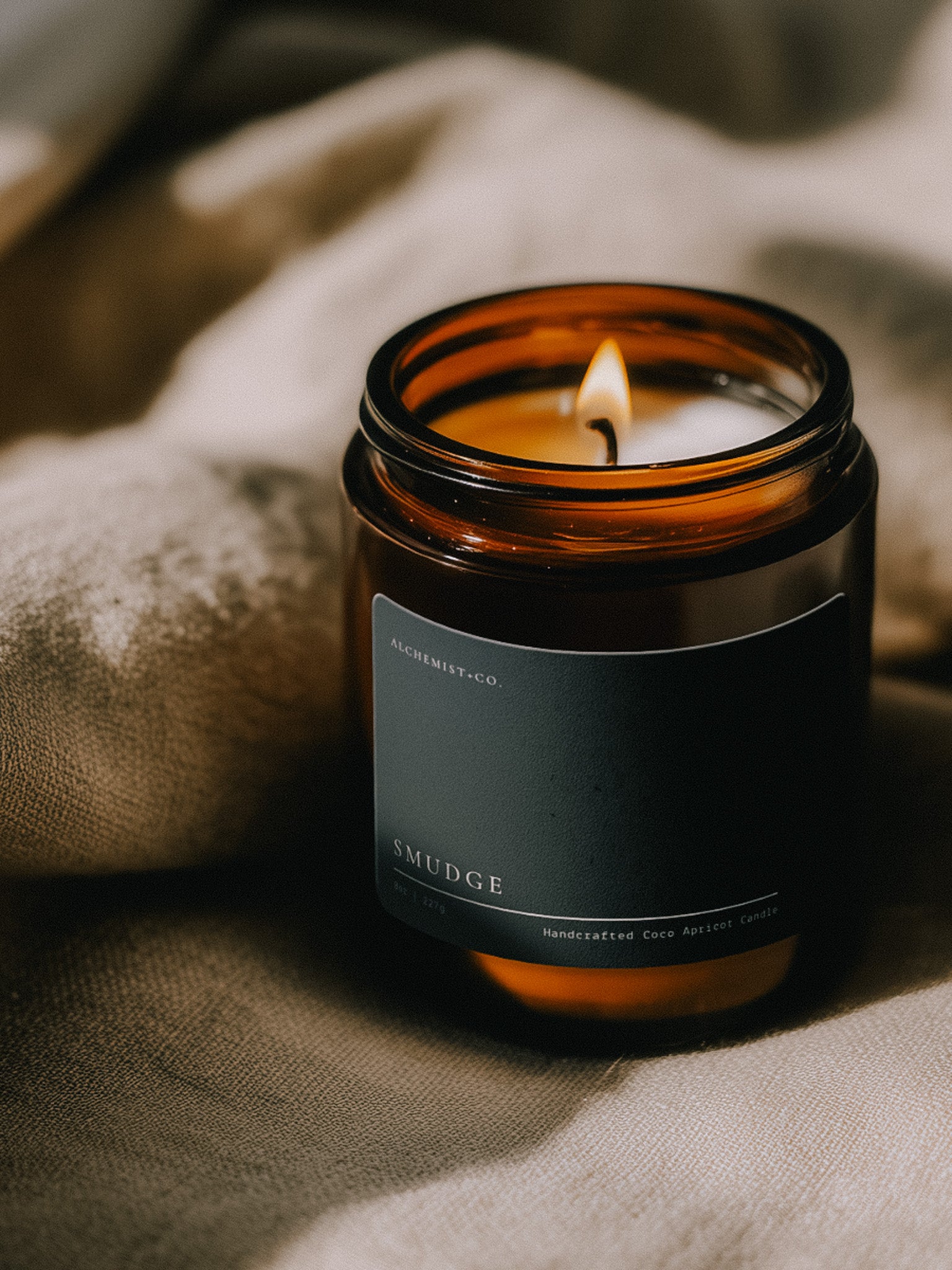 Lit Smudge ritual candle beside textured linen in warm atmospheric light.