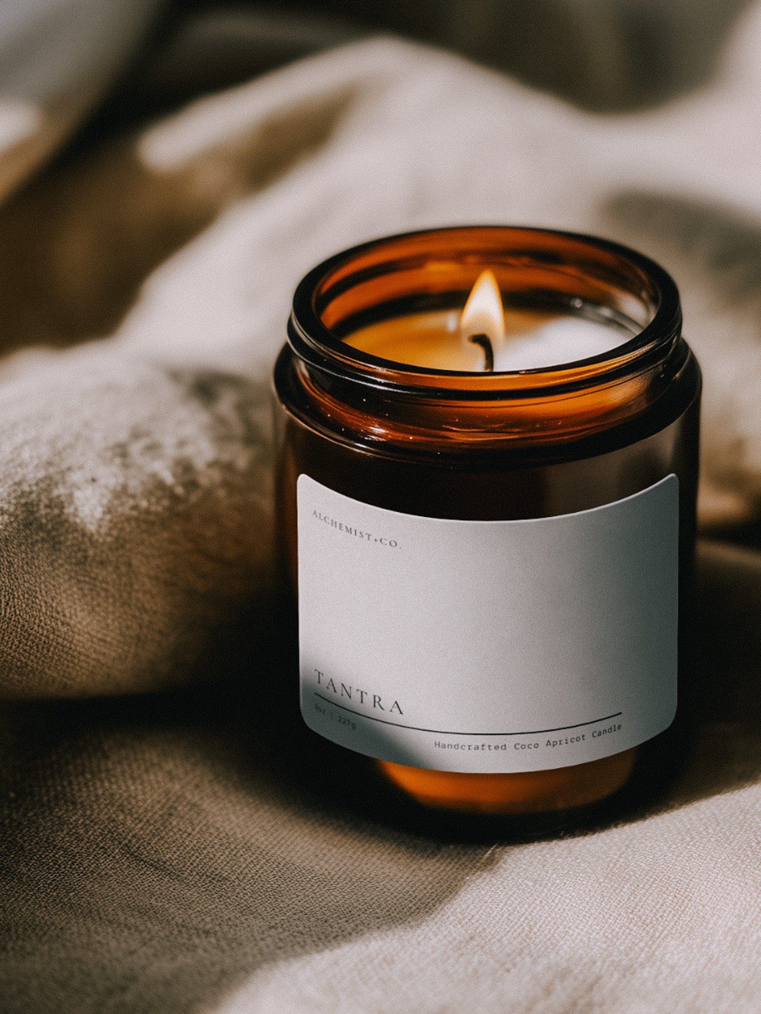 Lit Tantra ritual candle beside textured linen in warm atmospheric light.