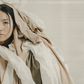 A Gemini woman covered in comfort blankets and clothing on a neutral background.