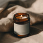 Teakwood + Patchouli Bare candle burning beside soft linen in warm atmospheric light.
