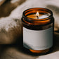 Lit The Fool ritual candle beside textured linen in warm atmospheric light.