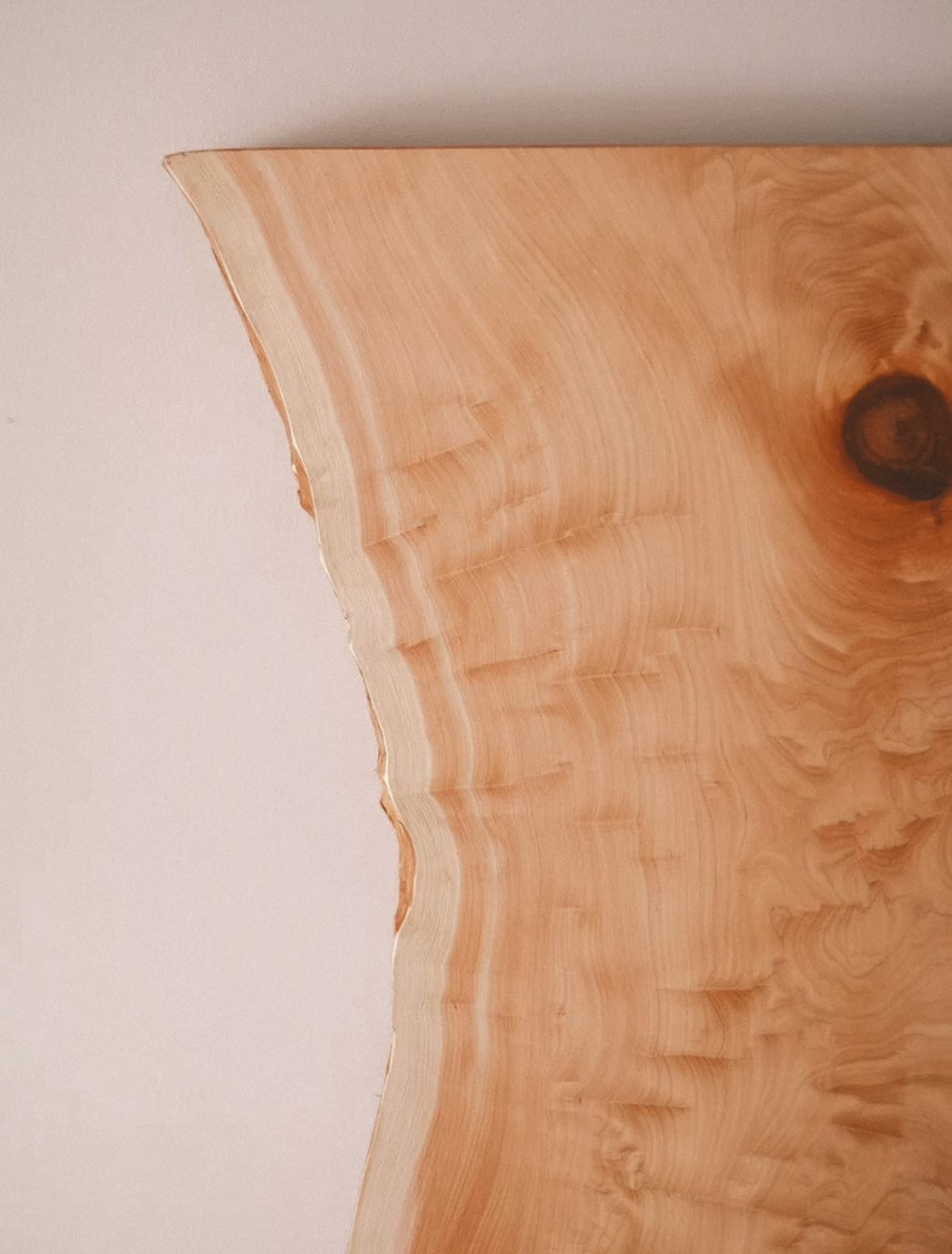 A pale live-edge wood slab with soft grain and a single dark knot, the hero note of the Threshold candle
