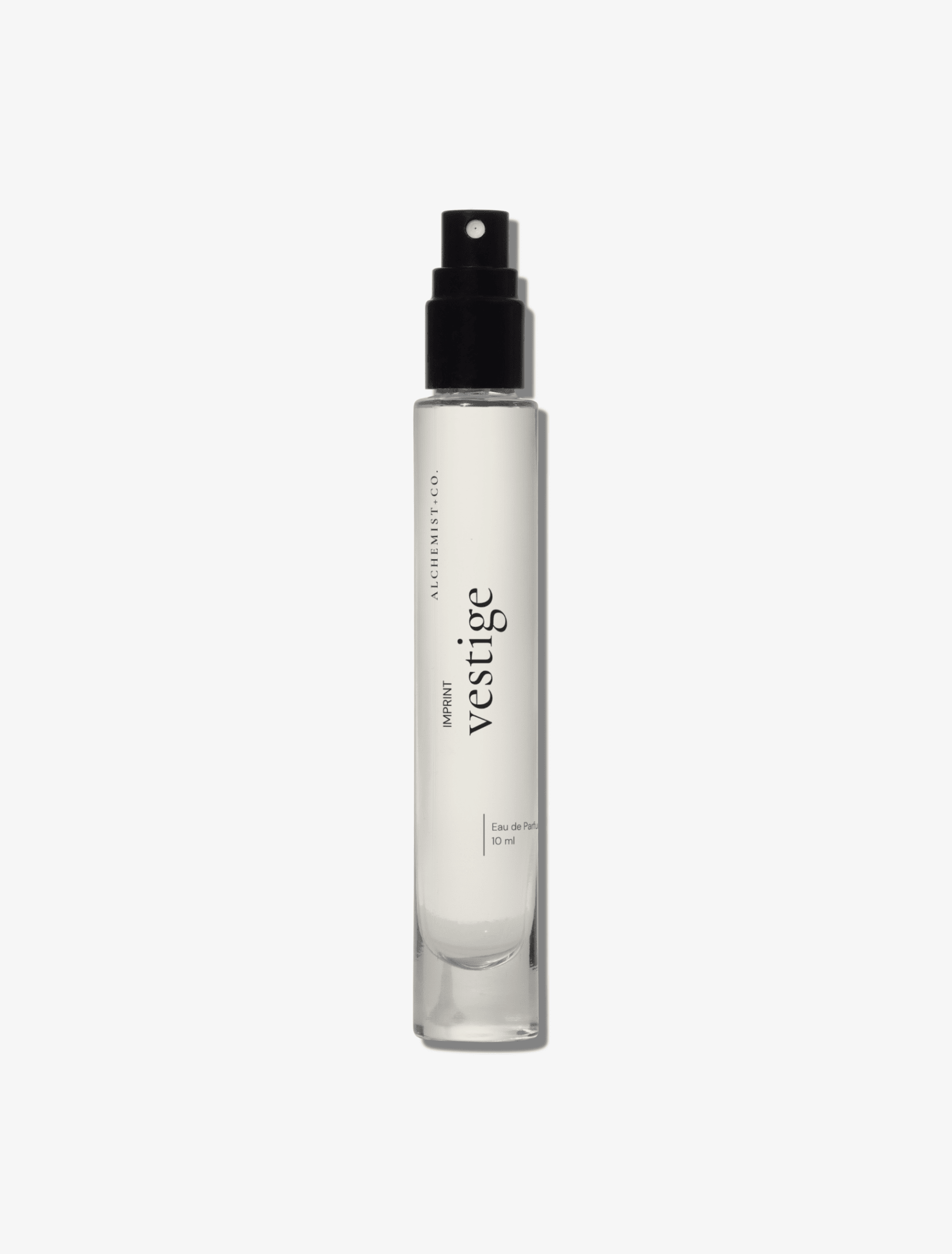 A clear glass perfume bottle featuring a white label with the brand name 'Vestige' by Alchemist + Co.  set against a solid light gray background.