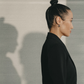 A stoic Virgo woman in a black blazer and a tight clean bun against a neutral background.