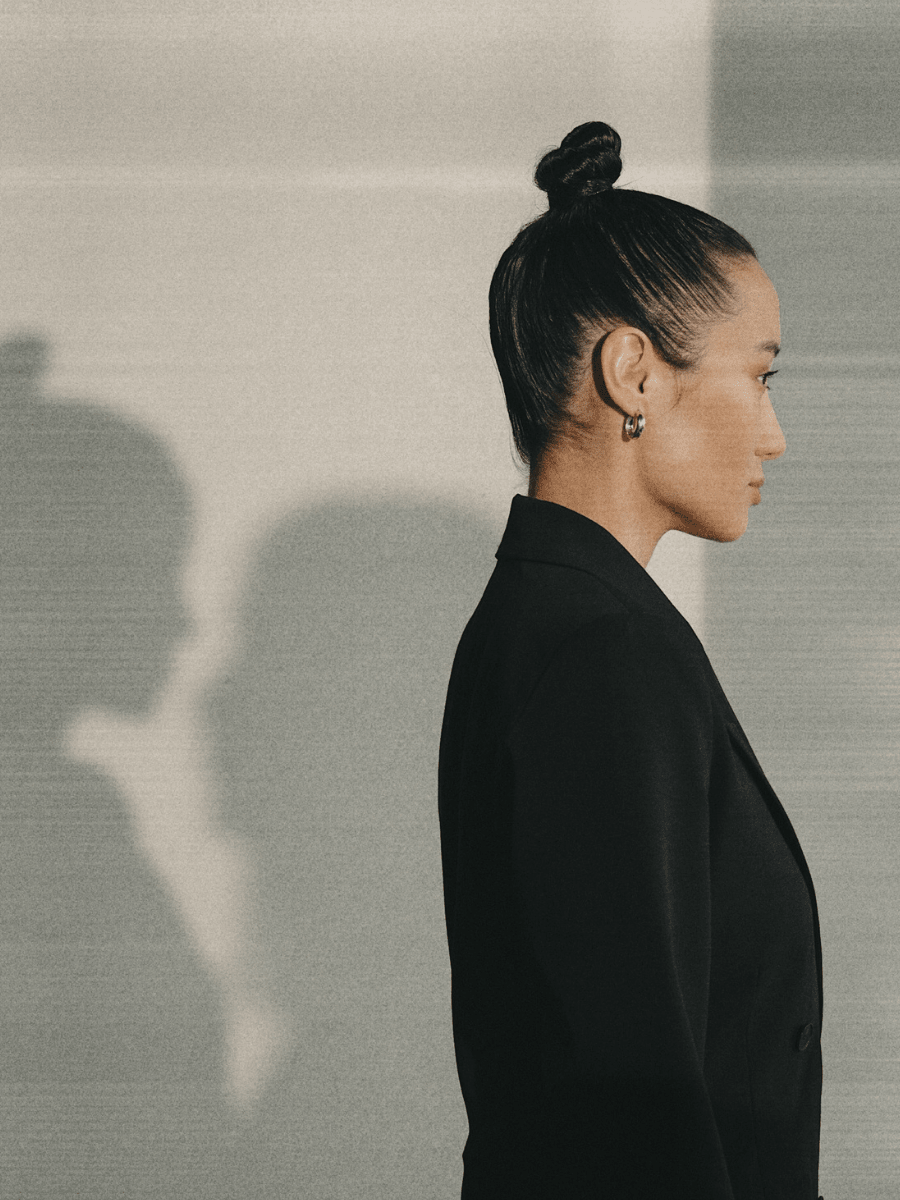 A stoic Virgo woman in a black blazer and a tight clean bun against a neutral background.
