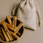 Bowl of Palo Santo sticks with a drawstring bag labeled 'Alchemist & Co.' on a beige background